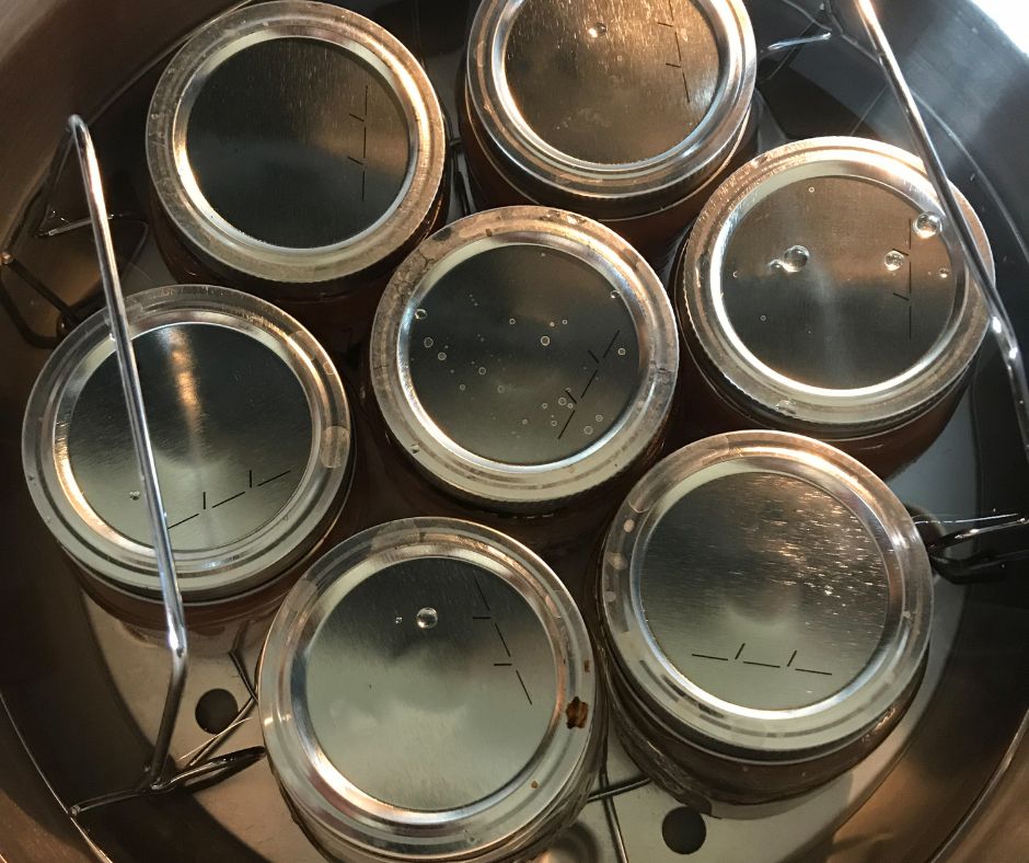 Several jars submerged in a hot water canning pot.