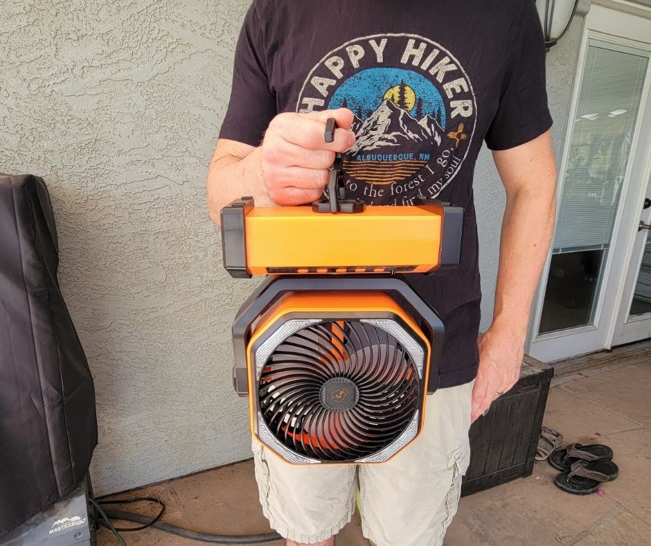 A man holding a battery powered fan by a built in hook.