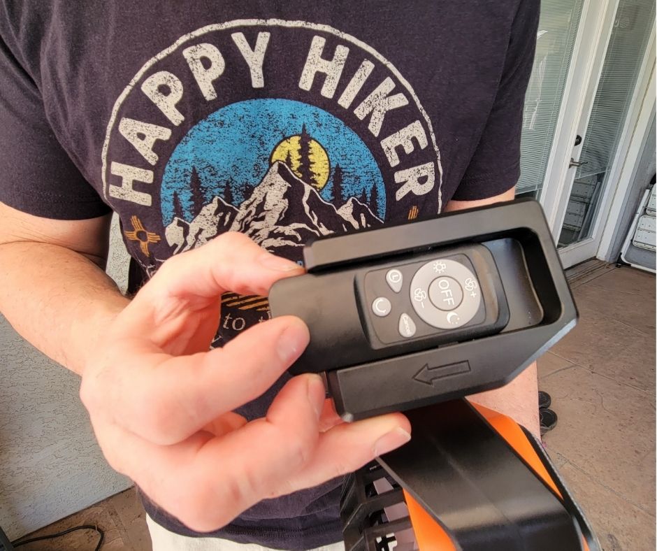 A man wearing a black happy hiker shirt hold a small remote control.