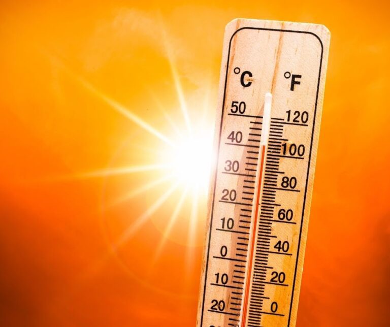 A thermometer held up to bright sun in a orange sky.