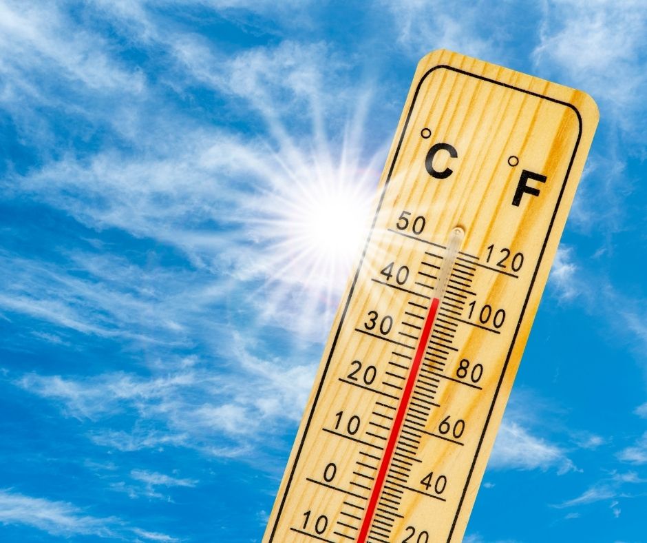 A thermometer held up to bright sun in a blue sky with a few white clouds.