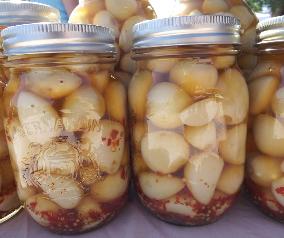 Canned jars of large white garlic cloves with a generous amount of red pepper flakes.