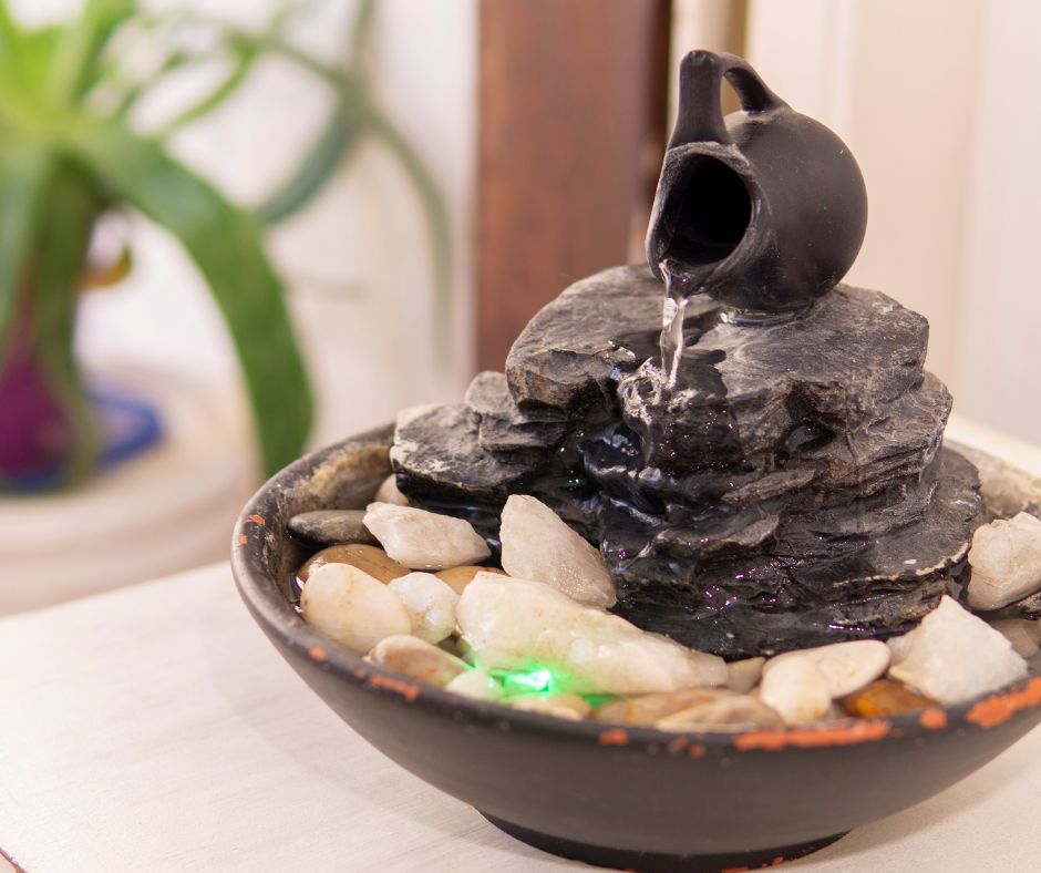 A small grey table top fountain made of stones with a small pitcher at the top.