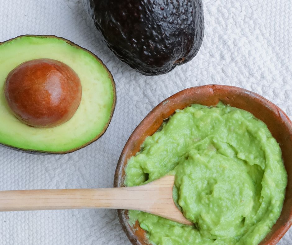 A bowl of bright green smashed avocado next to one sliced in half exposing the pit.