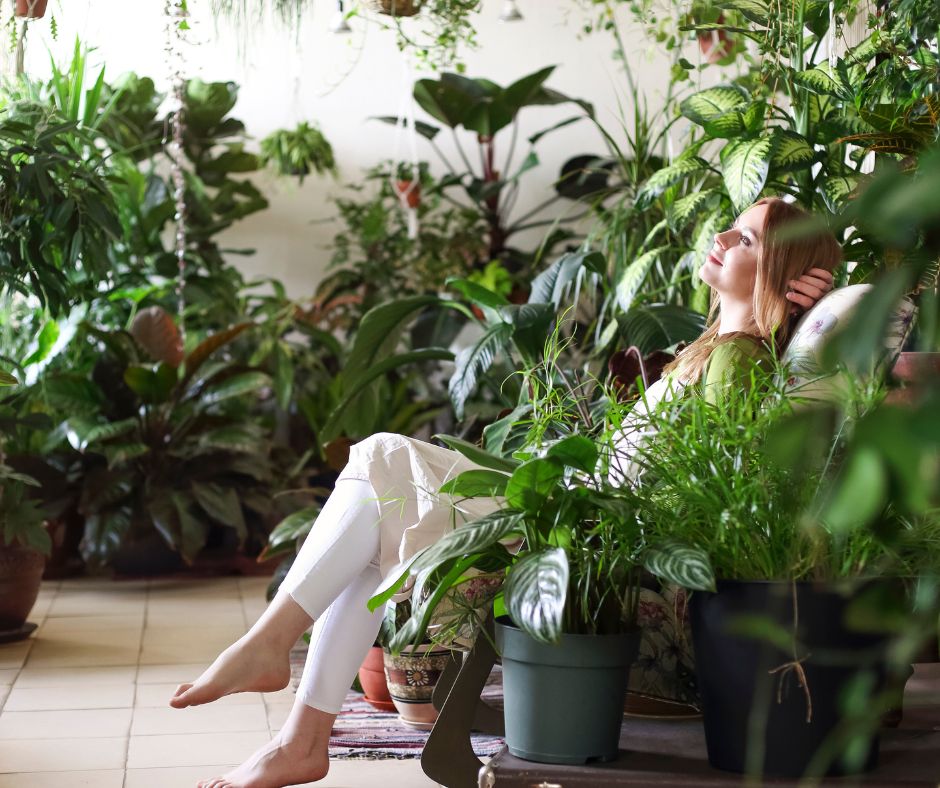A woman siting in a lush indoor garden full of plant of various sizes.
