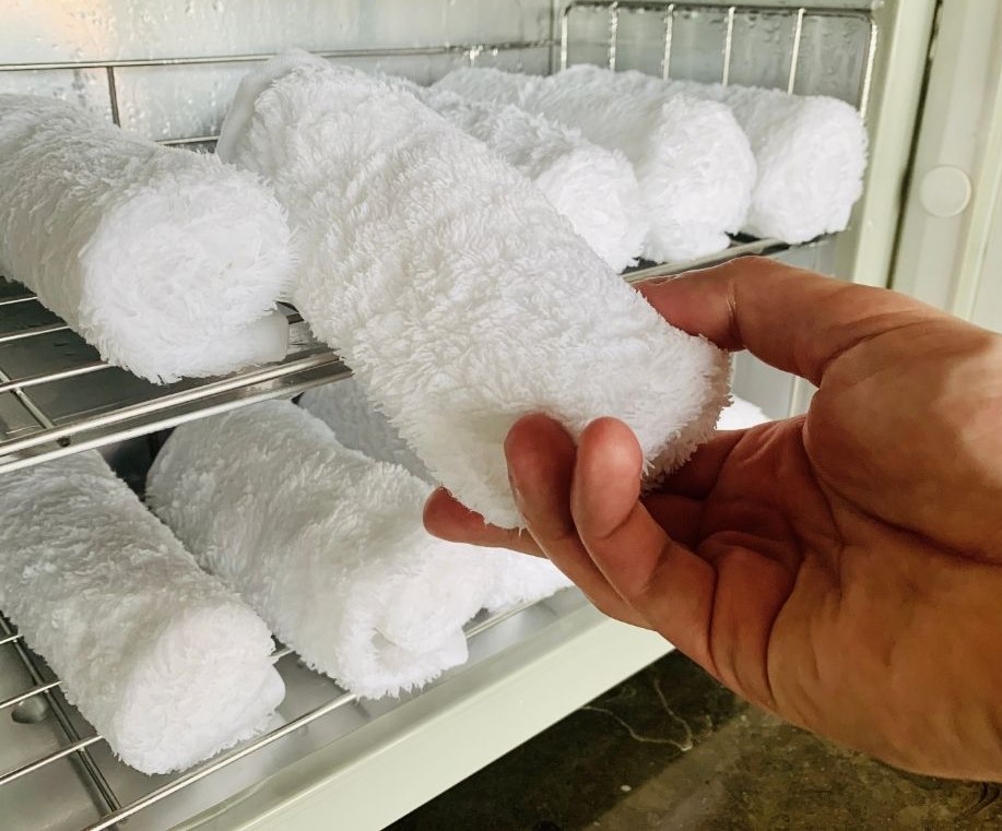 Rolled up white towels in a fridge. A hand removing one.