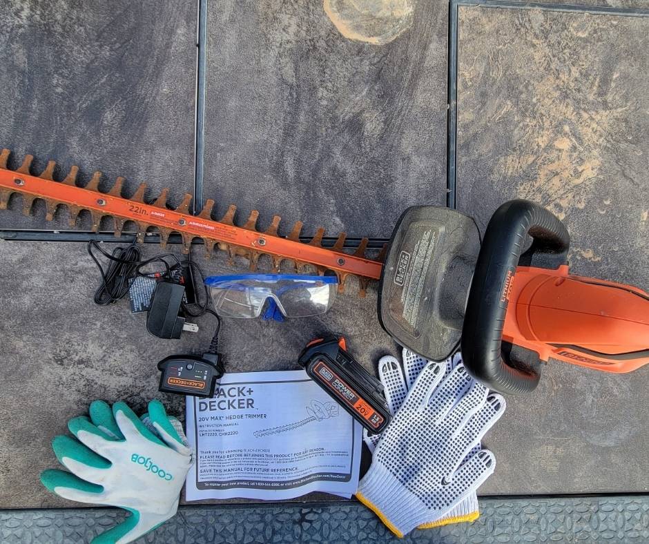 Gloves, cordless hedge trimmer, and guide book on an outdoor patio table.