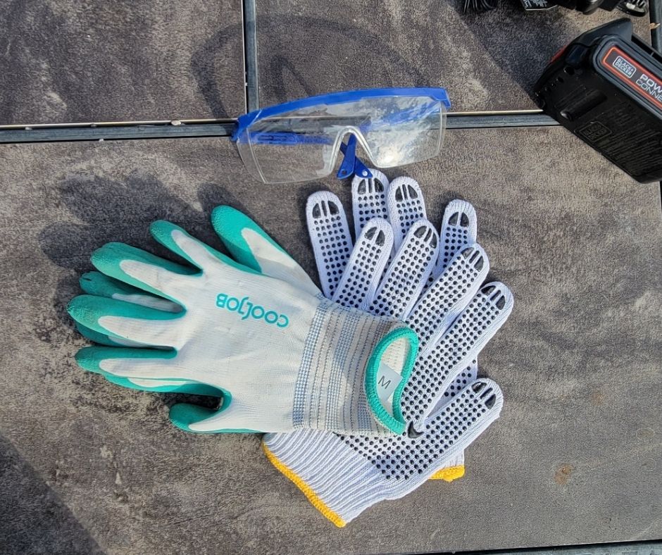 Two pairs of garden gloves and clear protective goggles on a patio table.