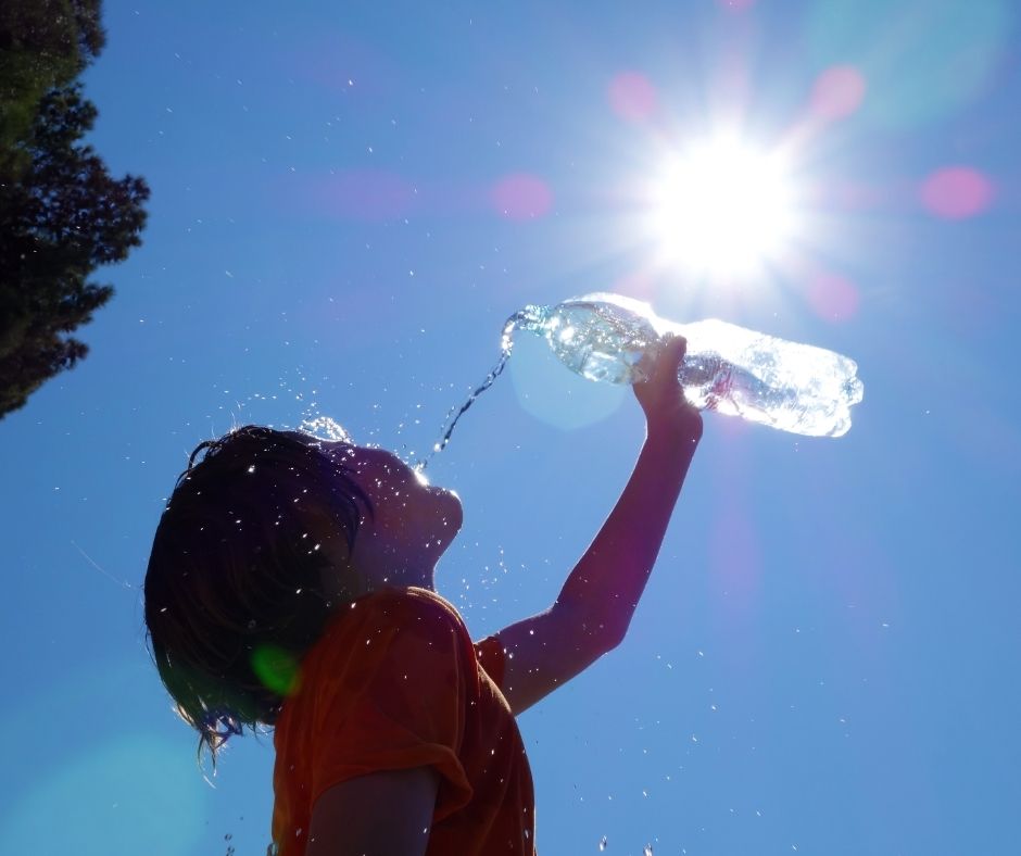A person pouring water over their face as a cooling solution on a hot sunny day.