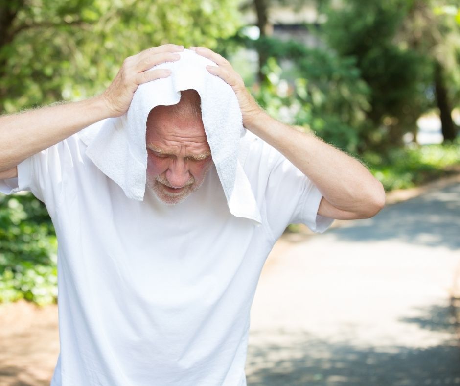 A man in a white shirt trying to cool down by placing a white towel on his head.