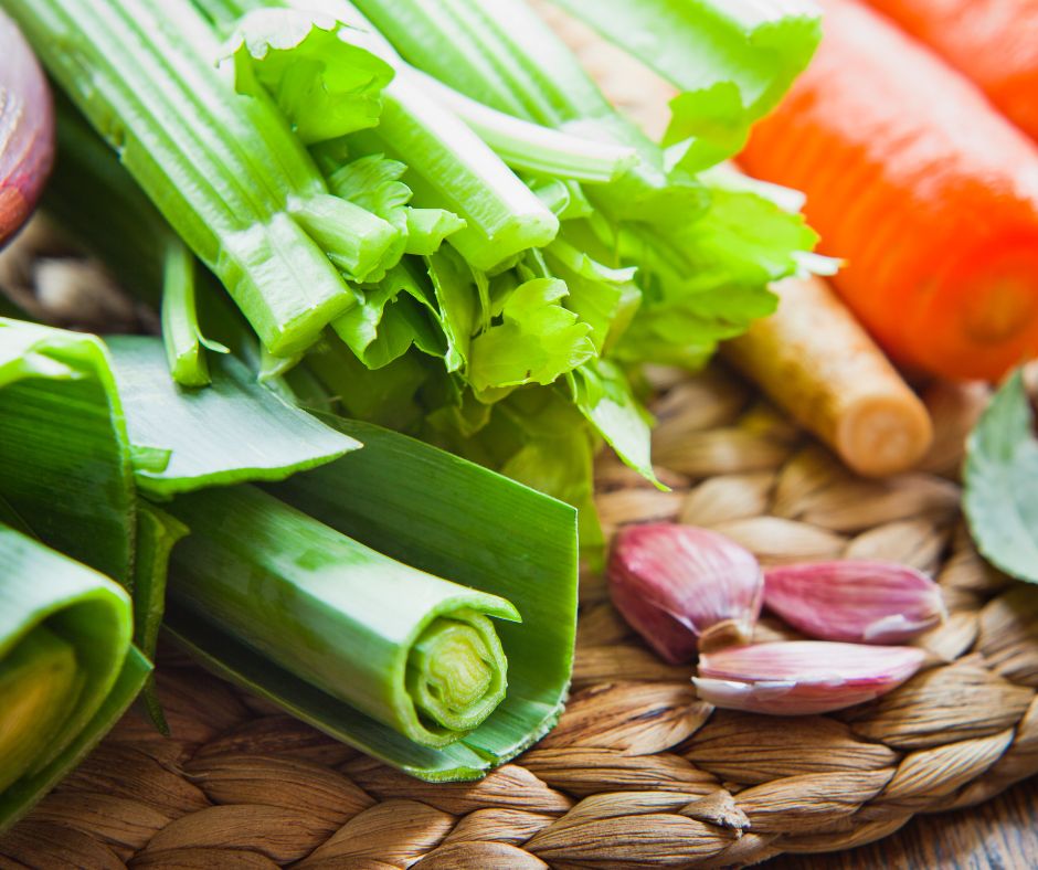 A collection of classic vegetable stock ingredients on a basket. Including green onions, garlic, carrots, celery, and bay leaves.
