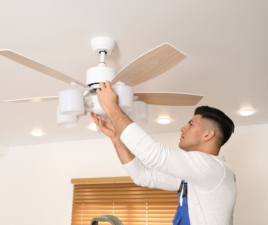 A man in a white shirt adjusting a ceiling fan.
