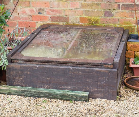 A dark wood garden cold frame with its transparent top closed.