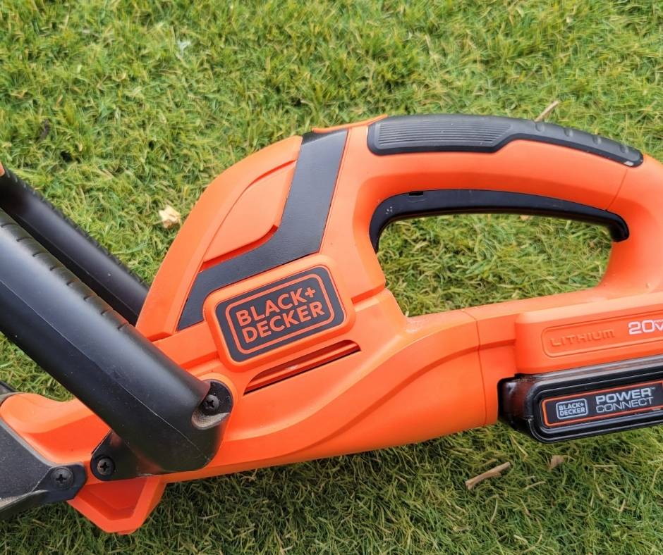 The orange body and black grip of a Black+Decker electric hedge trimmer.