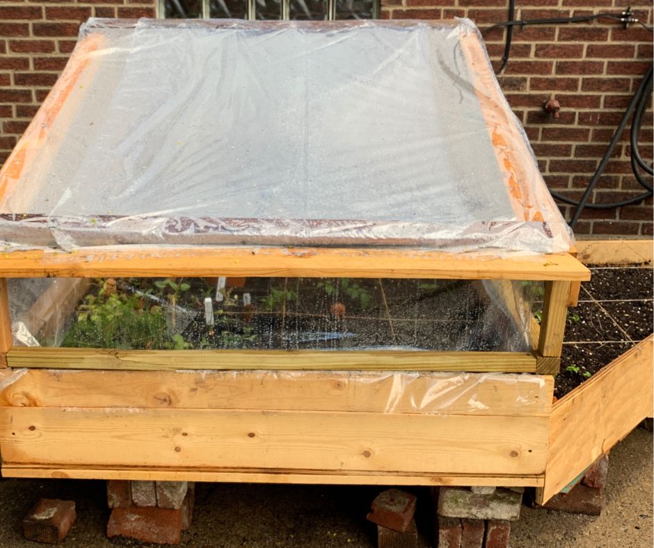 A raised wooden garden cold frame covered in clear plastic.