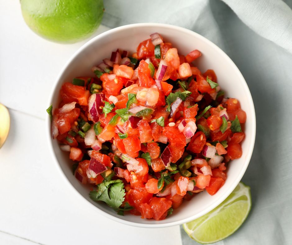Fresh chunky tomato salsa in a white bowl next to a lime wedge.
