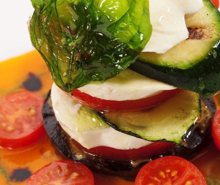 A fancy stacked Capri Salad in a dish of tomato broth and sliced cherry tomatoes.