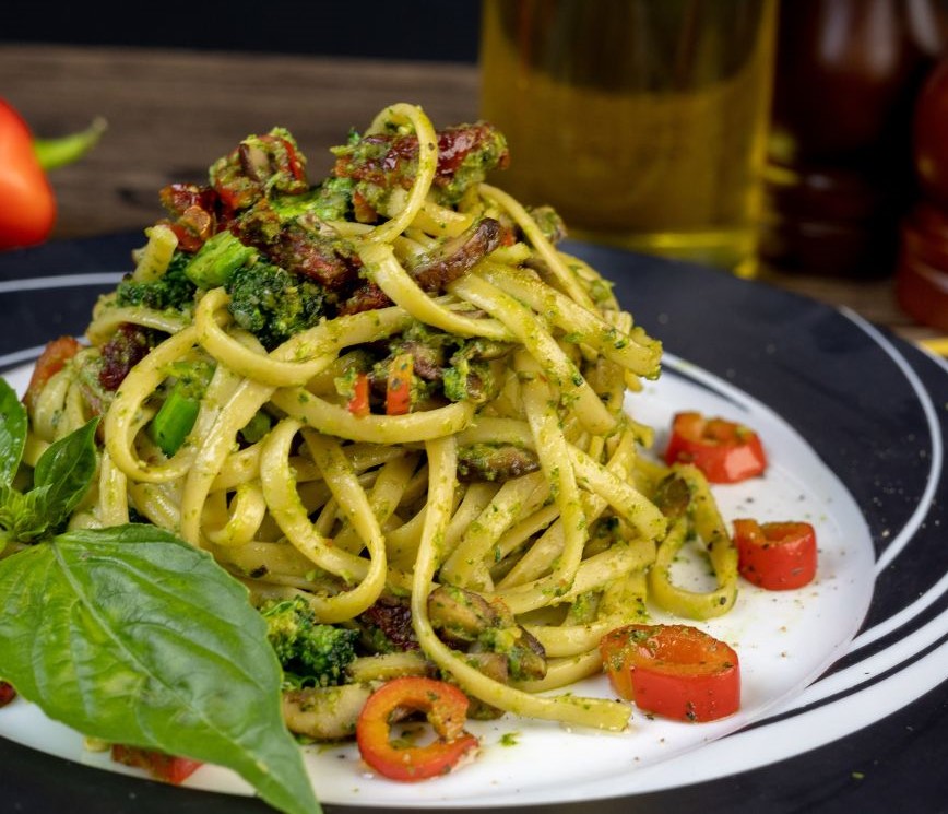 A place of pasta with a lot of green basil and fresh red tomatoes.