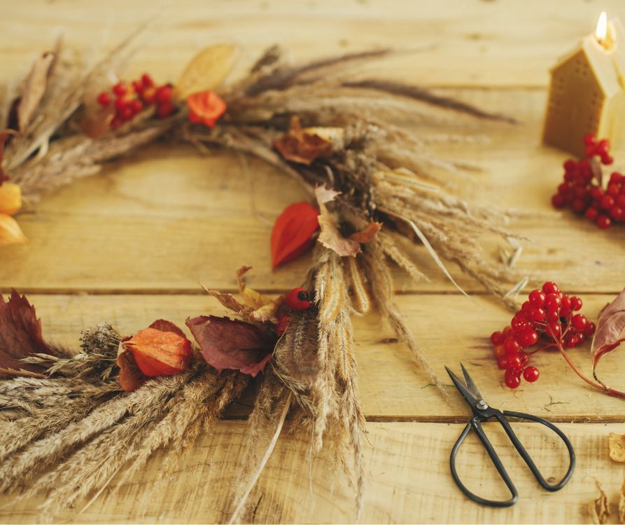 A Fall wreath made of dried grass and fall leaves on a work bench.