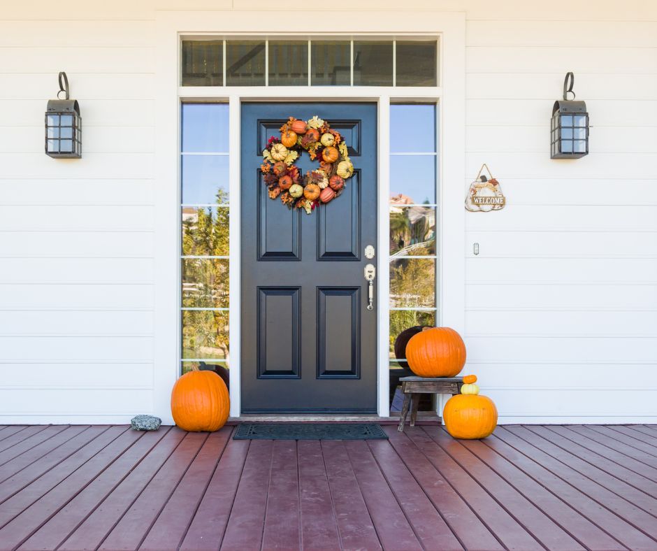 A black front door with a 3 orange pumpkins and a colorful fall wreath.