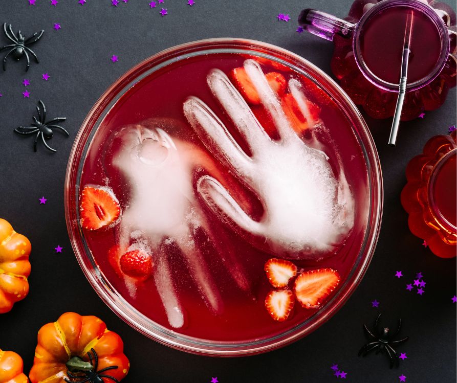 Hand shaped ice floating in red Halloween punch on a black table.