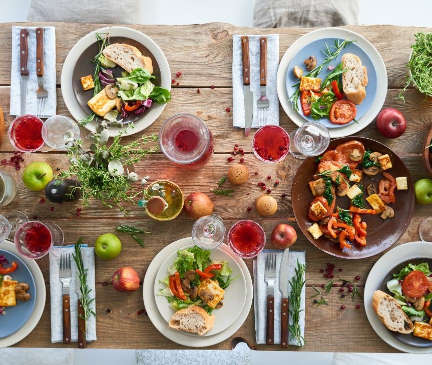 A wooden table set with a fall dinner theme. Including roasted chicken, veggies, and red drinks,