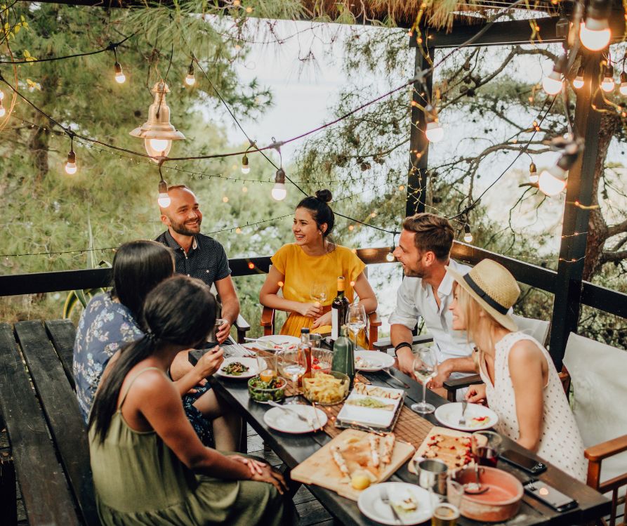 A group of people chatting and eating at a table under a pergola.