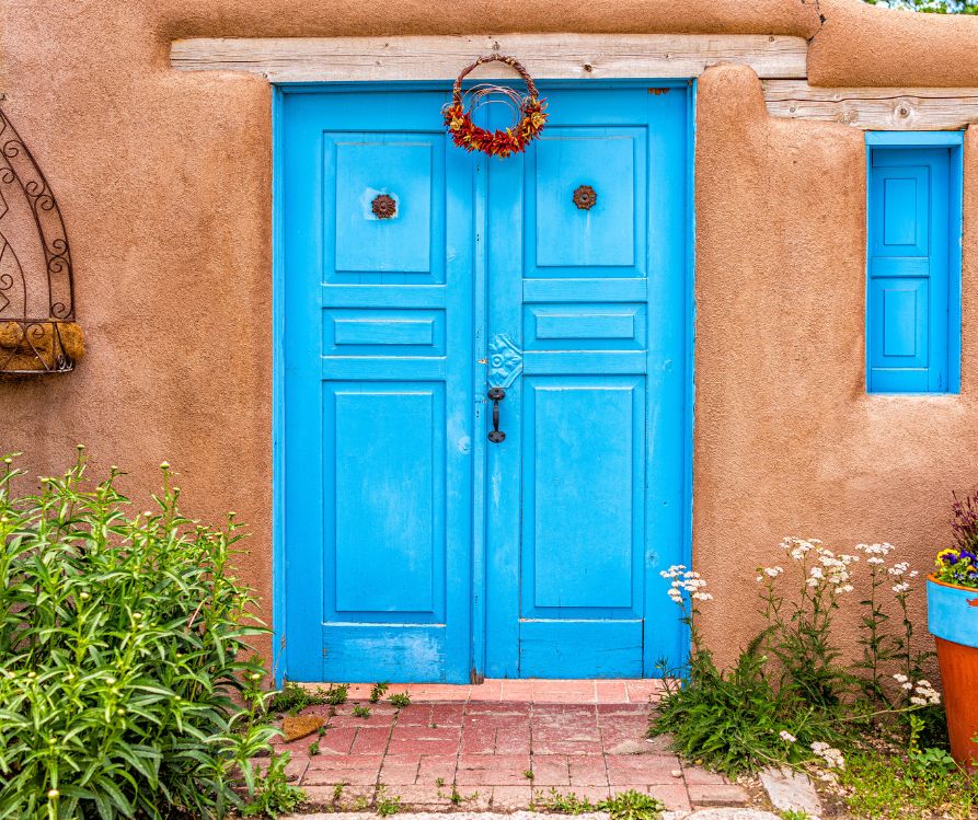 A blue door on an adobe building displaying a simple red chile wreath.