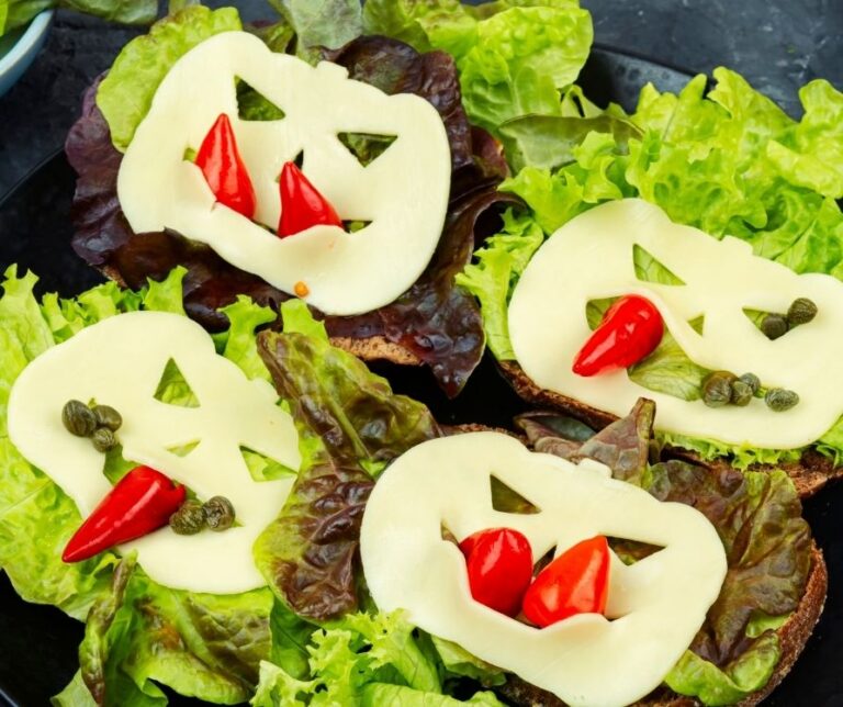 Open face sandwiches of green lettuce, cheese cut into jack o lanterns and red peppers and cappers.
