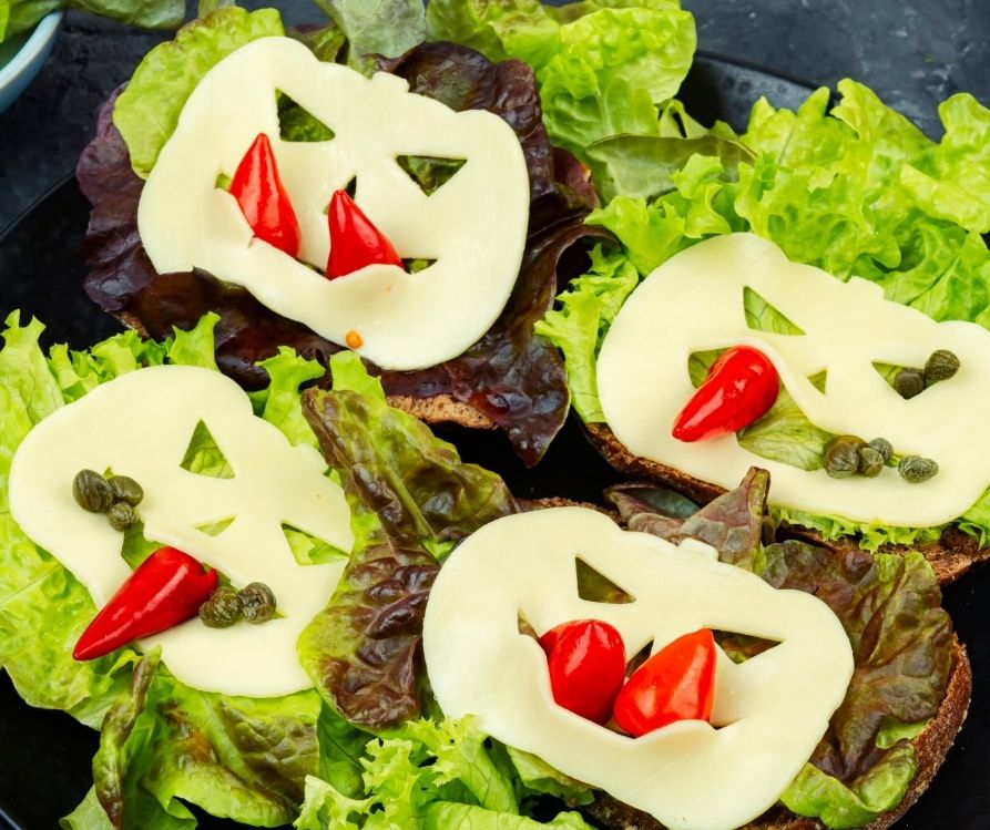 Open face sandwiches of green lettuce, cheese cut into jack o lanterns and red peppers and cappers.