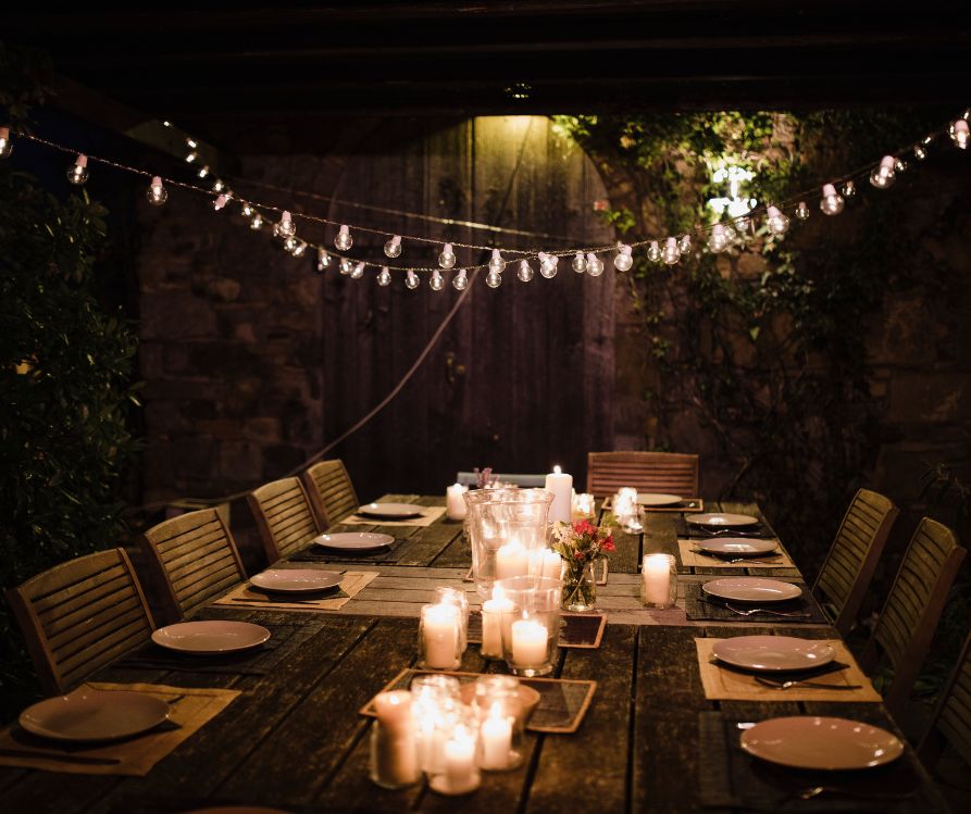 A long dinner table set with plates, candles, and string lights.