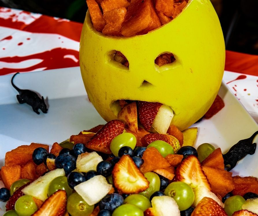 Melon with a face carved onto it and a mixed fruit salad in front of it.