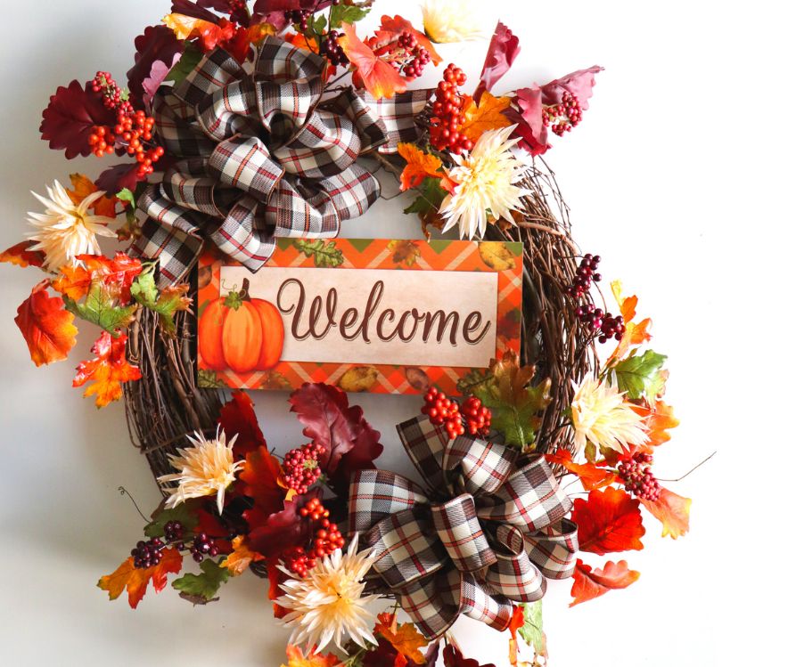 An Autumn wreath decorated with a wooden welcome sign and fall leaves and flowers.