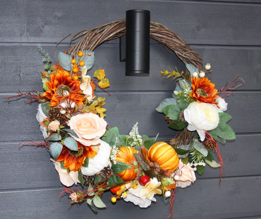 A grapevine wreath covered in flowers in a Autumn color pallet.