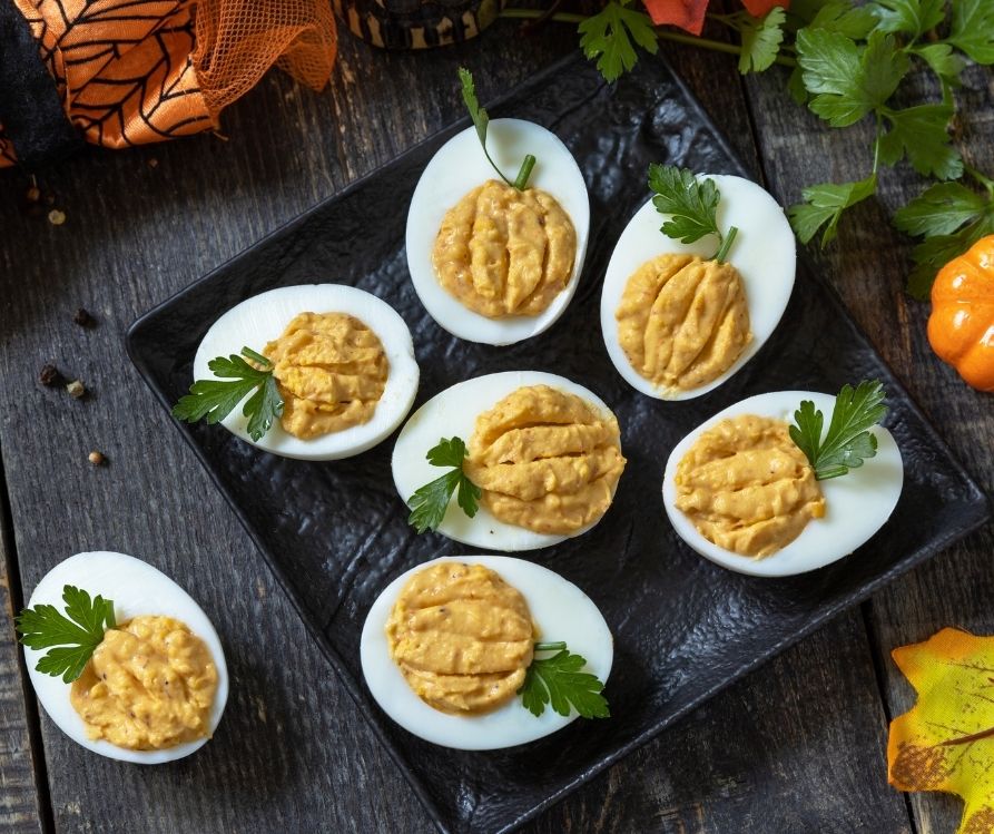 Deviled eggs with green garnish and filling pattern that resembles pumpkins