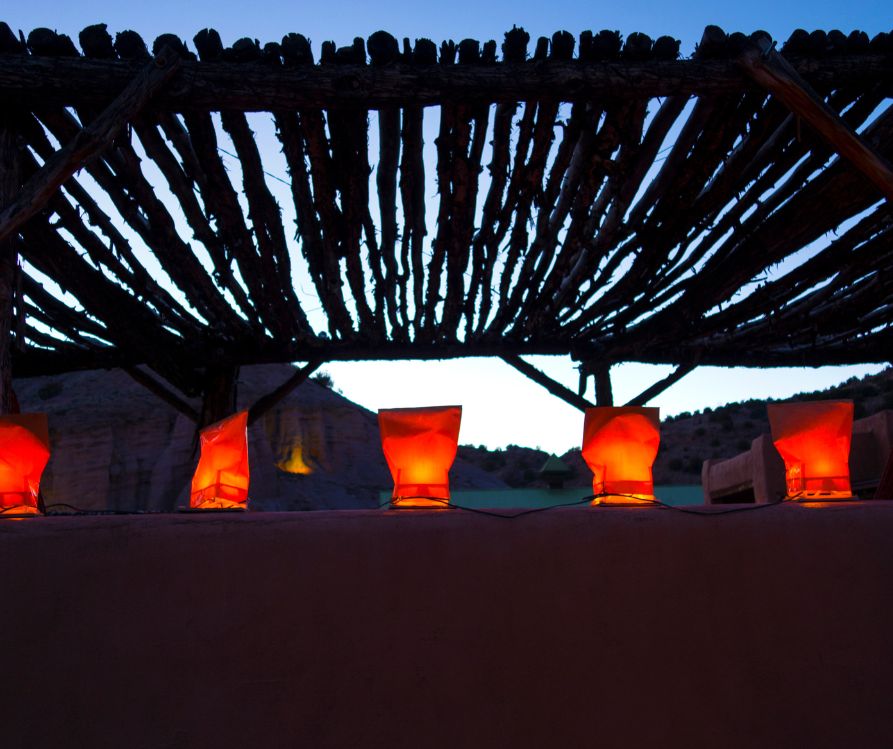 Farolitos lighting up an adobe wall next to an ocotillo branch pergola.