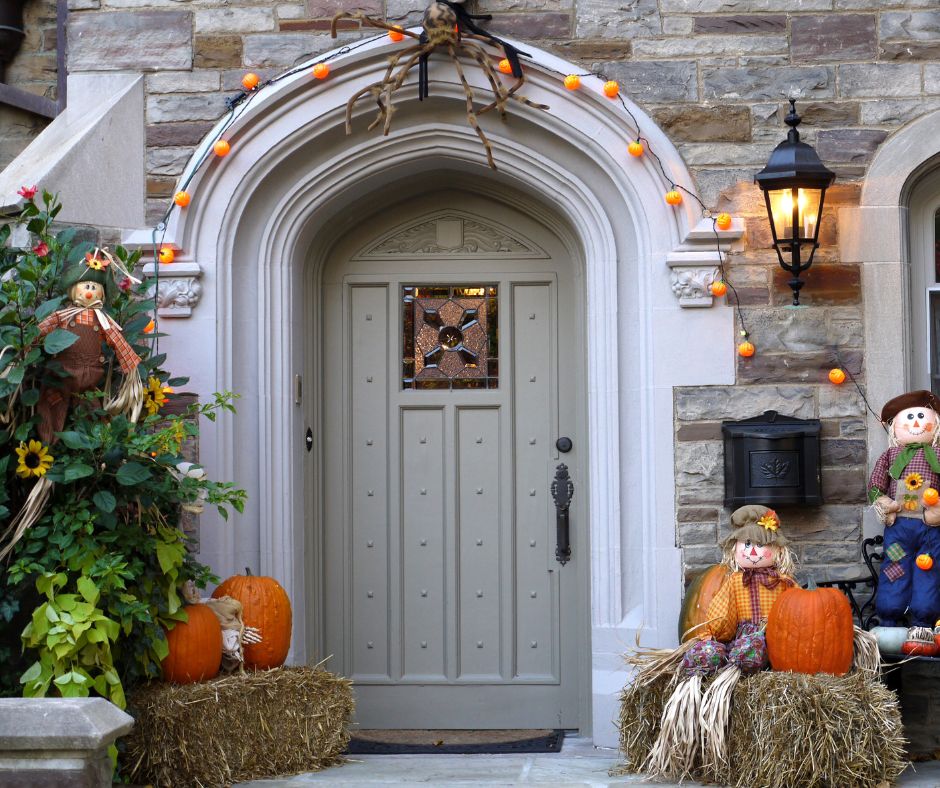 Straw bales, pumpkins and folky Halloween decorations frame a front door.
