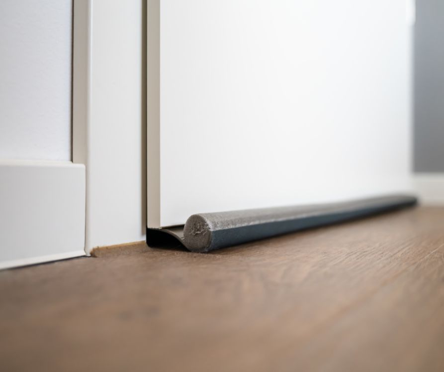 Grey draft stoppers blocking the gap below a white door.