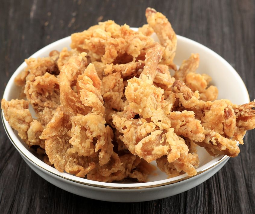 A white bowl of crispy fried oyster mushrooms on a wooden table.