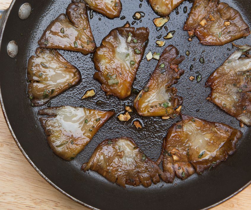 Oyster mushrooms sizzling in a cast iron pan with garlic and herbs.