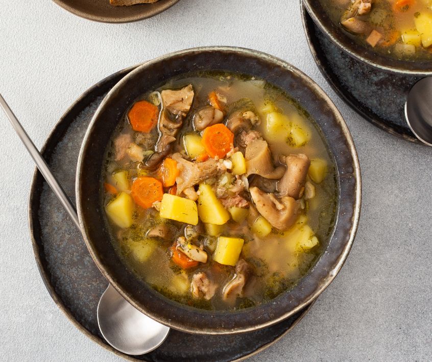 Mushroom and vegetable soup in dark ceramic bowls on a kitchen counter top.