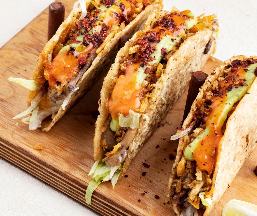 Three veggie and cheese tacos served on a wooden board.