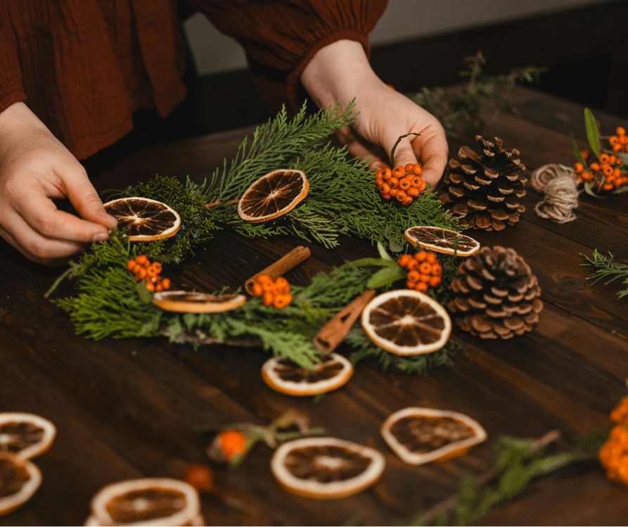 A person putting together holiday decorations made of home preserved fruit, spices, and garden clippings.