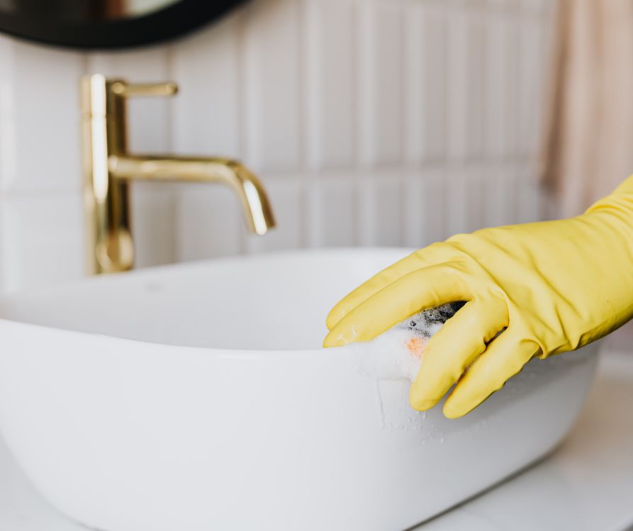 A person wearing yellow gloves cleaning a white sink.