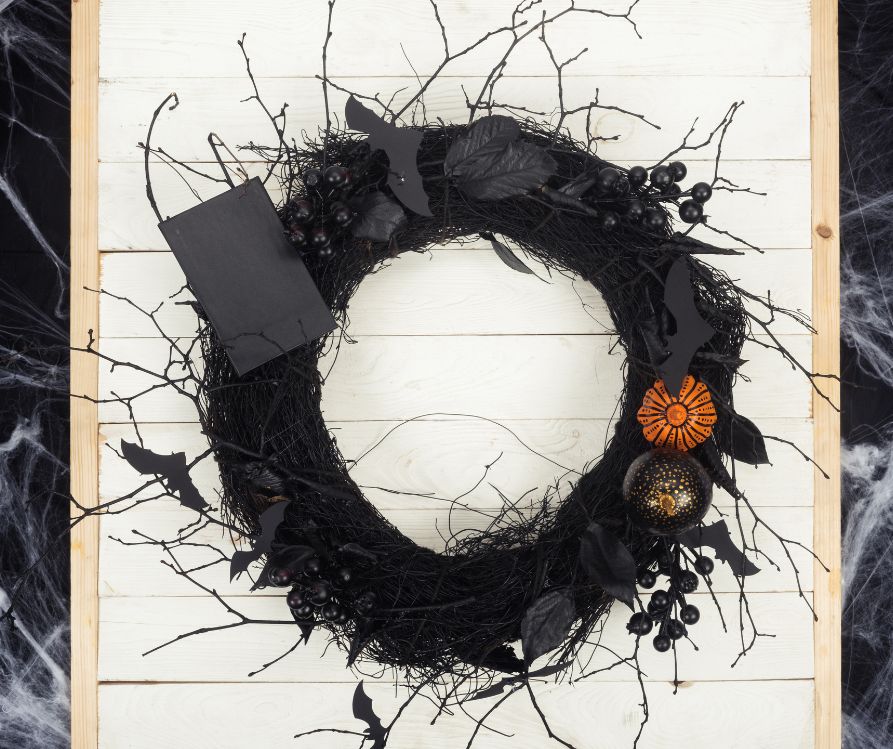 A black wreath covered in orange pumpkins, black bats, and thin crooked black twigs.