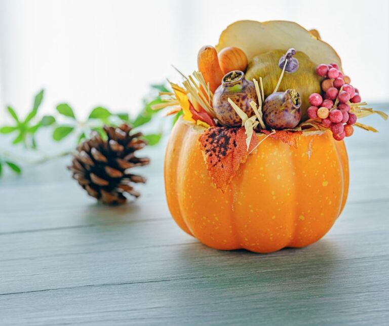 A small orange pumpkin used to hold autumn decorations on a blue table next to a pinecone.