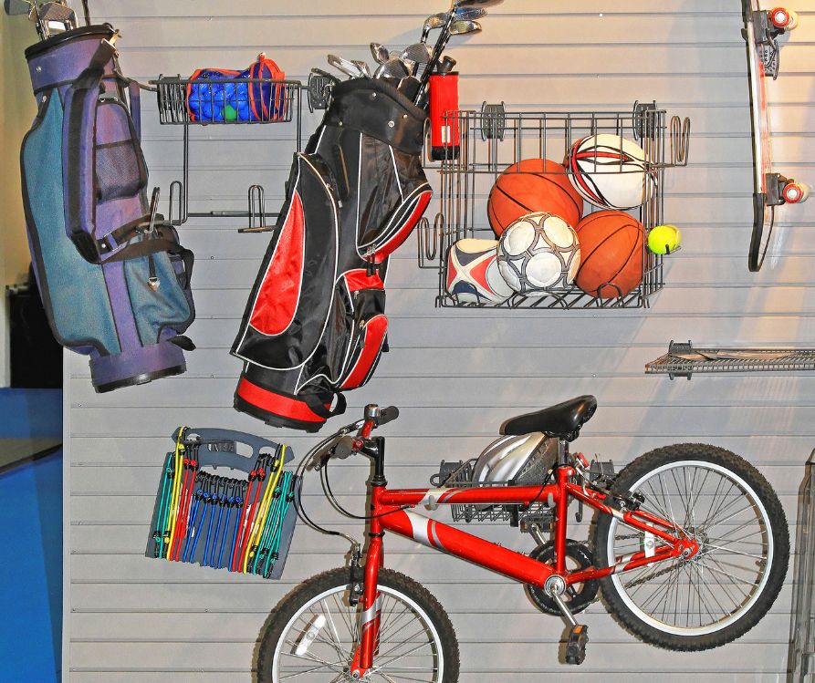 A bike, golf clubs, and balls hanging on a garage wall.