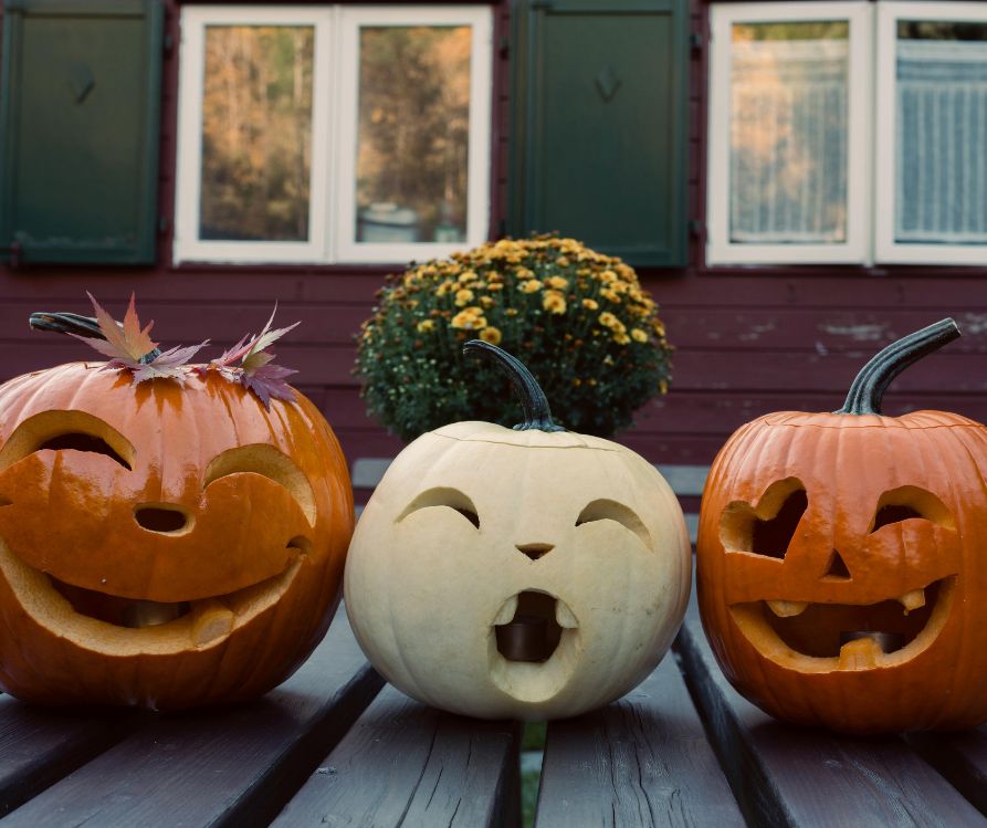 Two orange and one white jack-o-lanterns with fun faces carved into them.