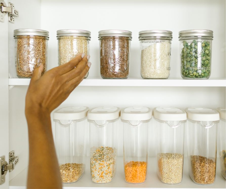 A person reaching for a jar in a white pantry with many jars in it.