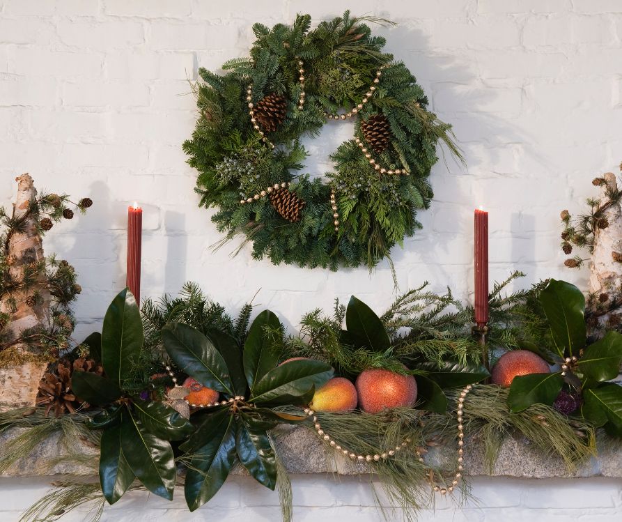 Local harvest themed holiday mantle decorations. Including big green magnolia leaves, citrus fruit, and candles.